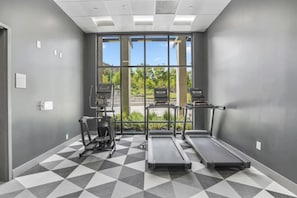 A gym with treadmills, an elliptical, and a stationary bike, with large windows and a geometric patterned floor. - Stadium/Events Suite Spot I Gym & Rooftop Lounge (Atlanta)