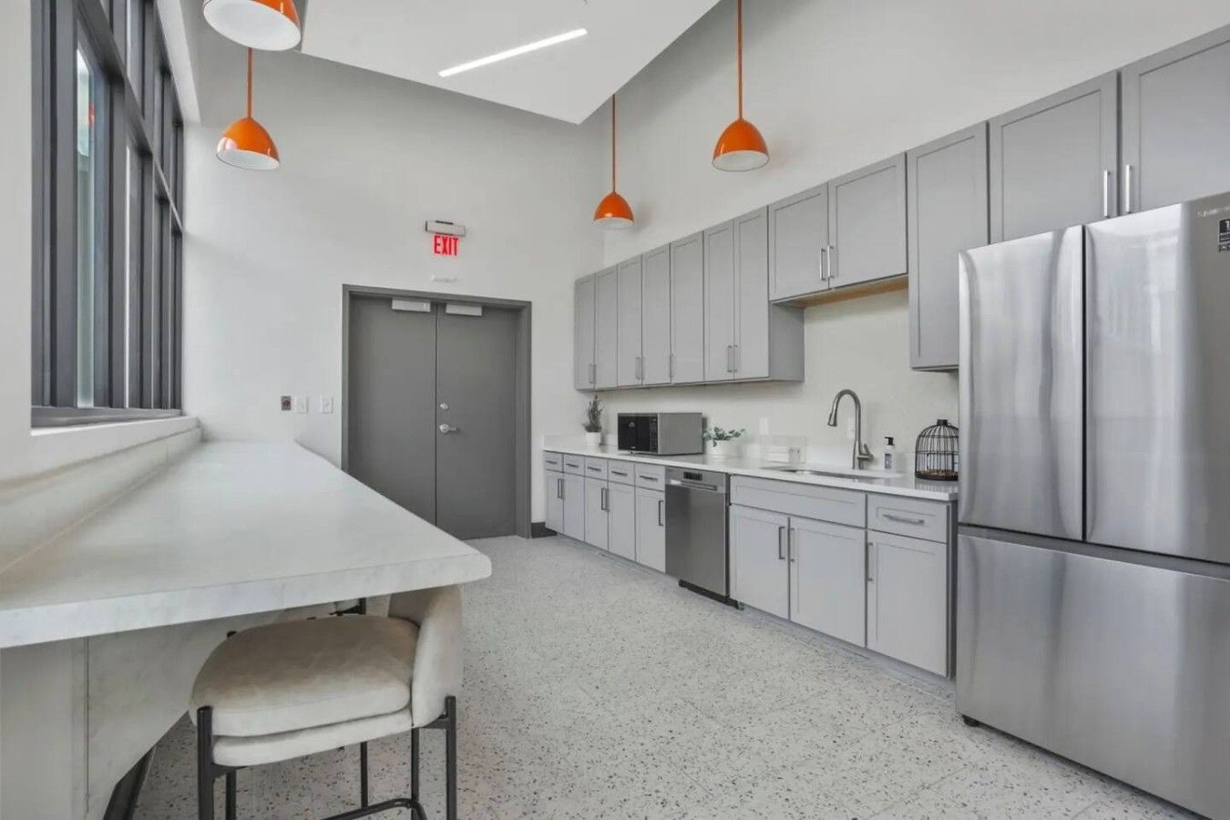 A modern kitchen with stainless steel appliances, grey cabinets, and pendant lighting.