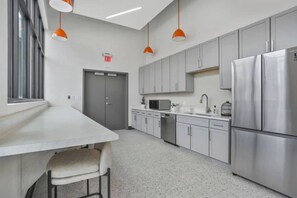 A modern kitchen with stainless steel appliances, grey cabinets, and pendant lighting. - Stadium/Events Suite Spot I Gym & Rooftop Lounge (Atlanta)