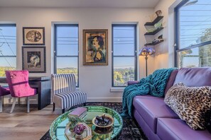 Uma sala de estar moderna com um sofá roxo, poltrona listrada e uma mesa de centro de vidro com objetos decorativos.