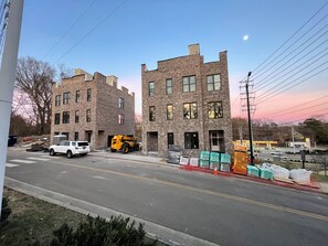A street view with two brick buildings, a white SUV, and a yellow construction vehicle. - NEW Cowgirl Brownstone near UT - 3 king suites, rooftop deck w Hottub (Knoxville)