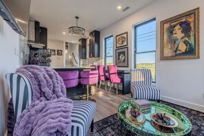 Uma sala de estar moderna com lareira, uma área de jantar com cadeiras cor-de-rosa e vista para o exterior por grandes janelas.
