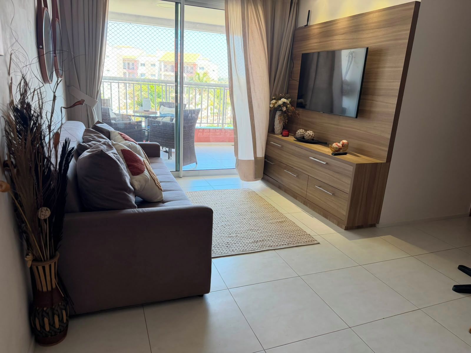 Una sala de estar moderna con un sofá, un televisor de pantalla plana montado en una pared de madera, y un puertas correderas de vidrio que dan a un espacio exterior.