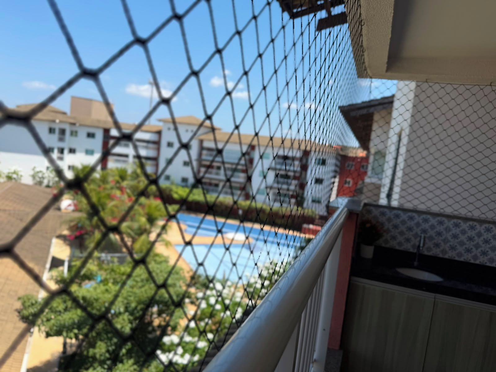 Una cerca de malla con vista a una piscina y edificios al fondo.