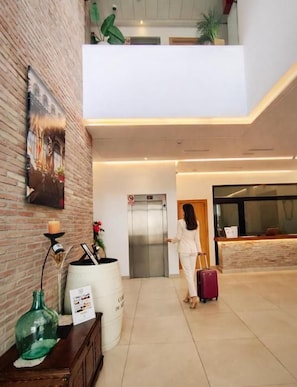 A lobby with a reception desk, a staircase, and a person with a suitcase. - Hotel-Restaurante Casa Marzo (Cariñena)