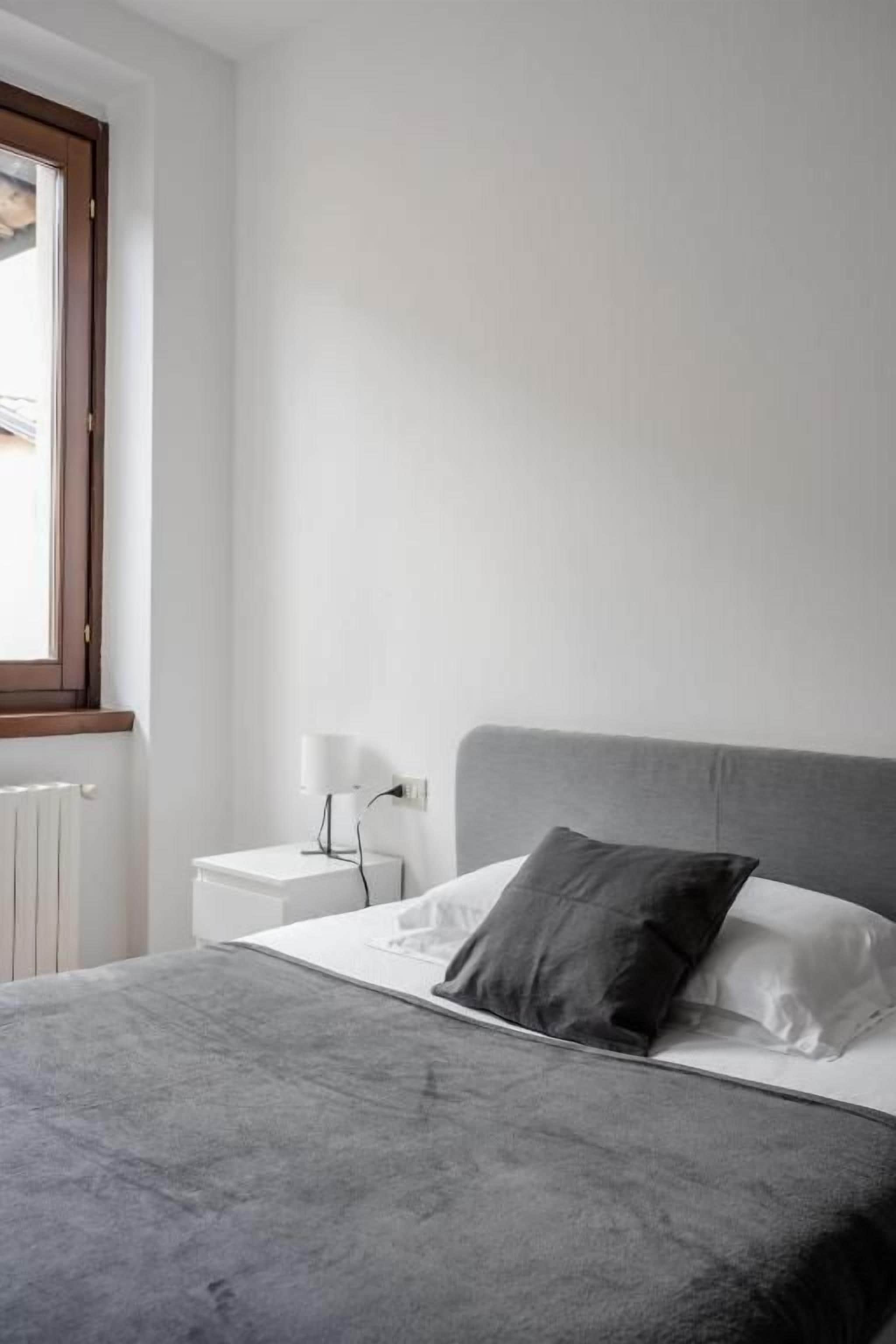 Une chambre à coucher avec un lit, une table de chevet, une lampe et une fenêtre.