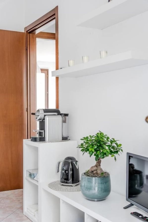 A modern living room with a coffee maker, a television, and a potted plant on a white console table.