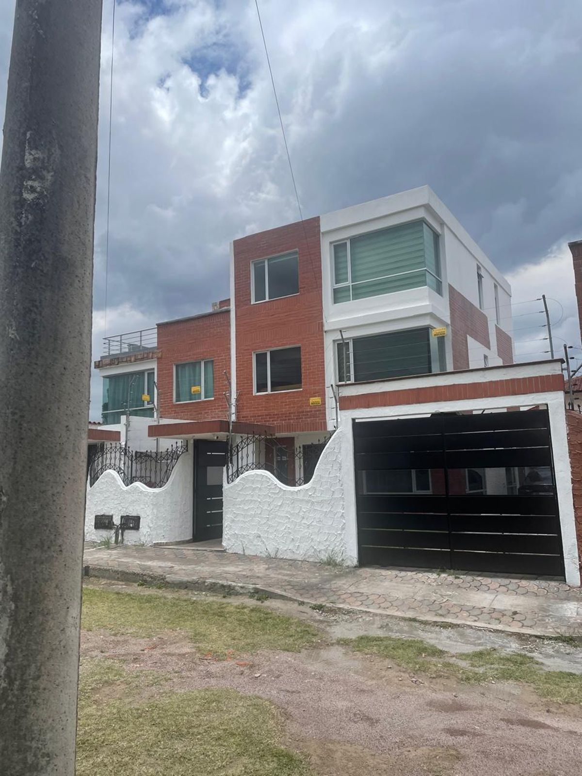 Edificio residencial de dos plantas con garaje, entrada protegida por un portón y camino de acceso pavimentado.