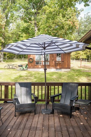 A wooden deck with two Adirondack chairs and a large striped umbrella. - The Sandbar at Sommer Dorf (West Branch)