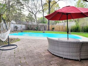 A backyard with a swimming pool, a wicker chair, and a red umbrella. - Galilea Sweet Home- 3 Bedroom, 2 Full Baths + Pool! (Houston)