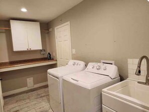 A laundry room with two front-loading washing machines, a sink, and a cabinet above the machines. - Galilea Sweet Home- 3 Bedroom, 2 Full Baths + Pool! (Houston)