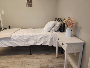 A bedroom with a bed, a nightstand, a wall-mounted decoration, and a wooden floor. - Galilea Sweet Home- 3 Bedroom, 2 Full Baths + Pool! (Houston)
