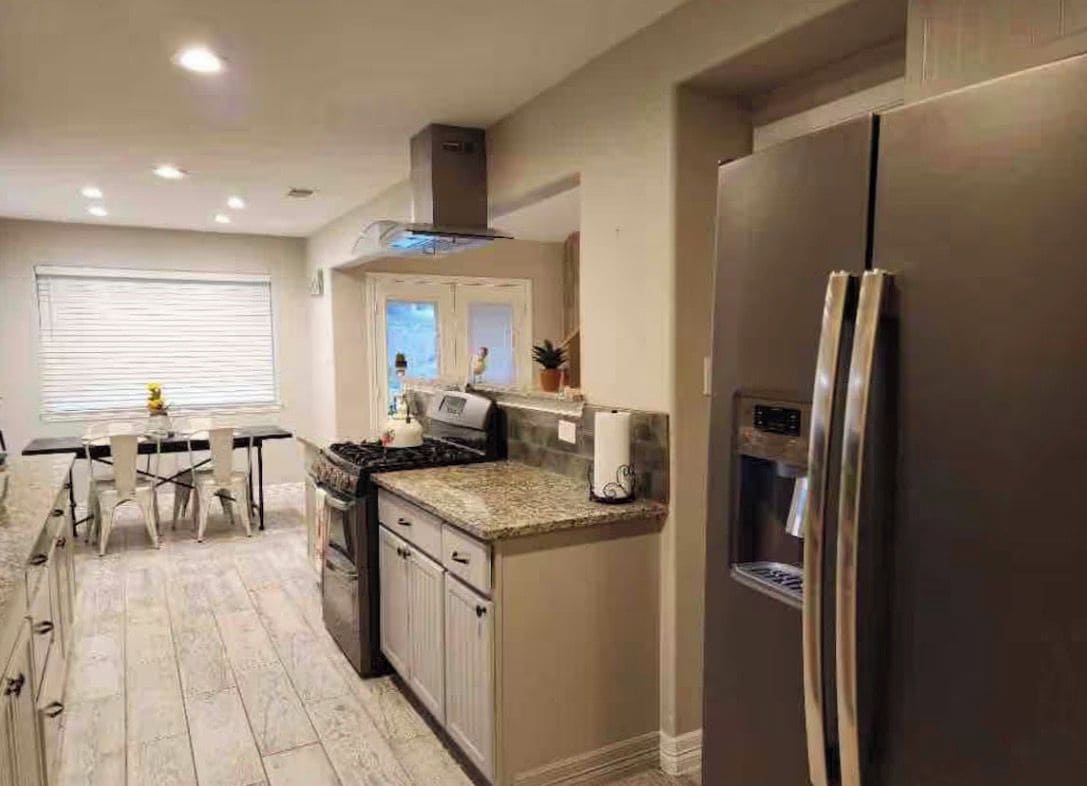A modern kitchen with a stainless steel refrigerator, a built-in oven, and a dining area with a table and chairs.