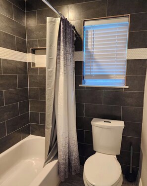 Ein Badezimmer mit einer Badewanne, Toilette und einem Fenster mit Jalousien.