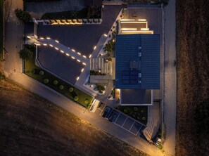 An aerial view of a modern building with a parking lot, a landscaped garden, and a series of lights outlining the property. - Elegant 2-bedroom suite with private terrace in Pollenzo, Langhe and Roero (Pollenzo)