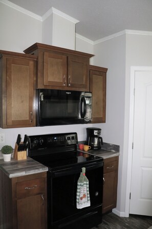 A kitchen with wooden cabinets, a black microwave, a stove, and a coffee maker.