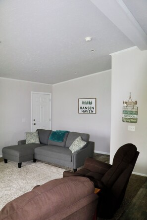 A living room with a gray sectional sofa, a brown armchair, and a white door.
