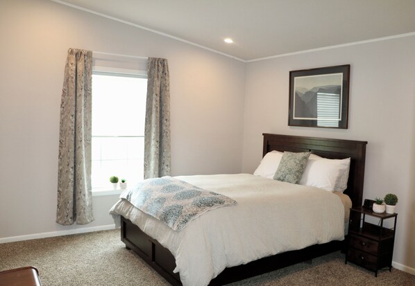 A bedroom with a bed, a nightstand, a window with curtains, and a framed picture on the wall.