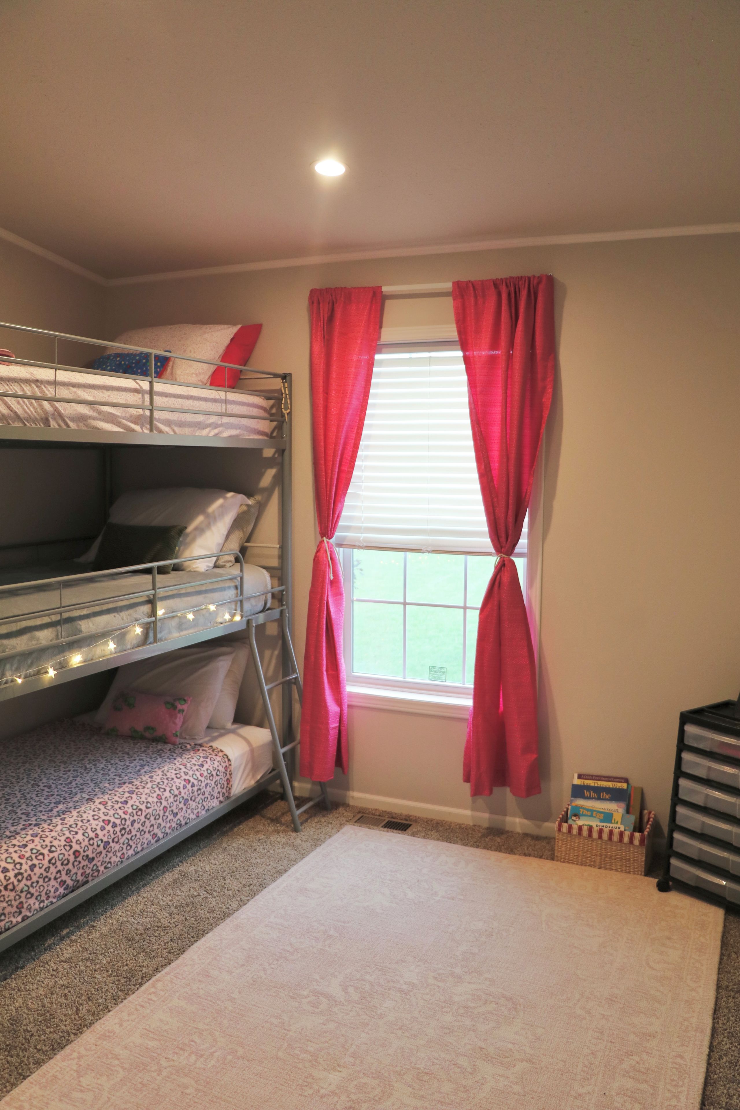 Quarto com beliche, janela, cortinas e unidade de armazenamento.