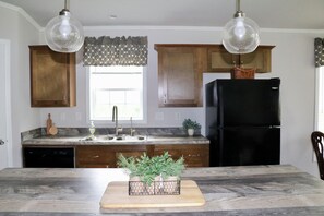 Cozinha com armários de madeira, geladeira preta, bancada de mármore e iluminação pendente.