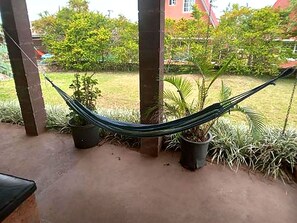 A hammock between two pillars in a covered outdoor area with potted plants and a grassy lawn. - D Monte Alto (ALTO BOQUETE)