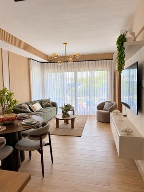 A modern living room with a sofa, dining table, chairs, a coffee table, and a TV mounted on the wall. - Lovely 2-bedroom apartment with AC in vibrant Punta Cana (Punta Cana)