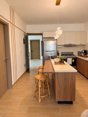 Une cuisine moderne dotée d’un îlot central, d’appareils électroménagers en acier inoxydable et d’un luminaire suspendu.