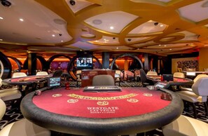 Ein Casino-Spielbereich mit mehreren Tischen, Stühlen, einem roten Teppich und einem auffälligen Deckenstil.