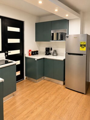 Una cocina moderna con armarios verde oscuro, un refrigerador de acero inoxidable, una cafetera y un microondas.