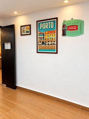 A hallway with a black door, a framed picture of Porto, and a Coca-Cola refrigerator. - Las Minervas residencias (Monterrey)