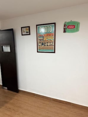 Un pasillo con un cuadro enmarcado de Oporto, una puerta y un cartel de Coca-Cola en la pared.