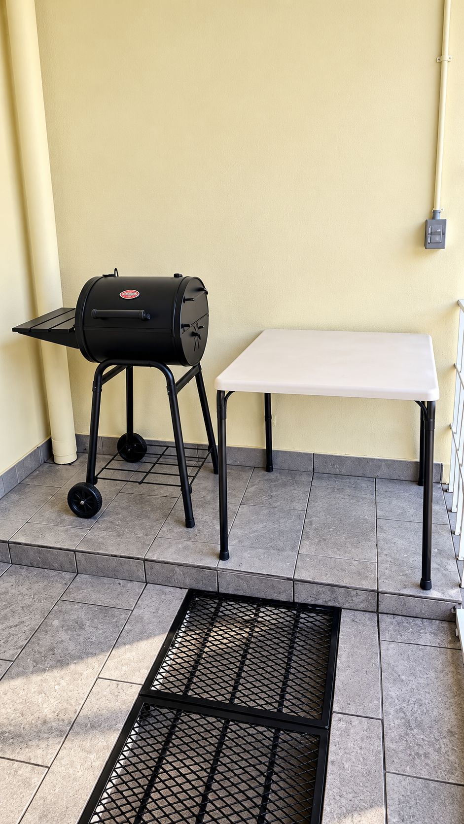 Una parrilla de barbacoa y una mesa blanca en un patio con baldosas.