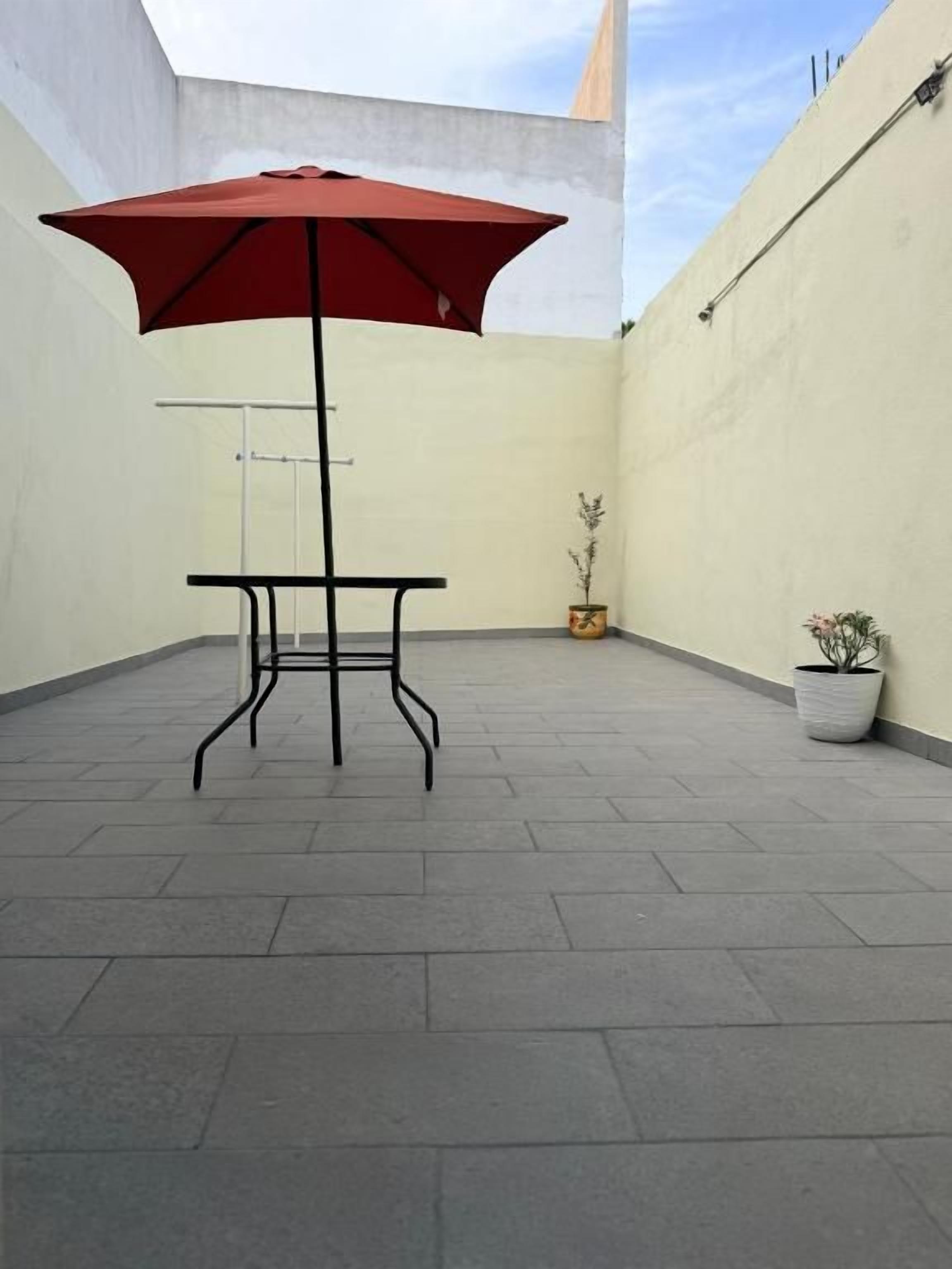 Un patio al aire libre con una mesa, un paraguas, una planta en maceta y una pared.