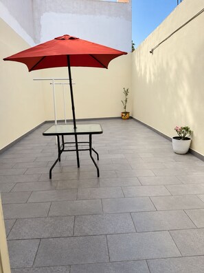 A patio area with a table and a red umbrella, surrounded by potted plants. - Las Minervas residencias (Monterrey)