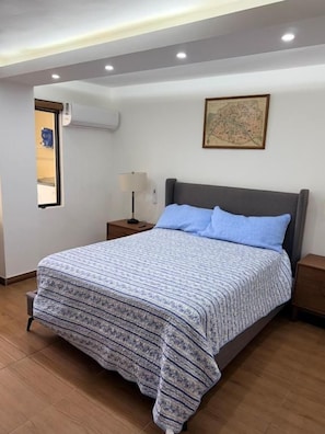 Un dormitorio con una cama, una mesita de noche, una lámpara y un aire acondicionado instalado en la pared.