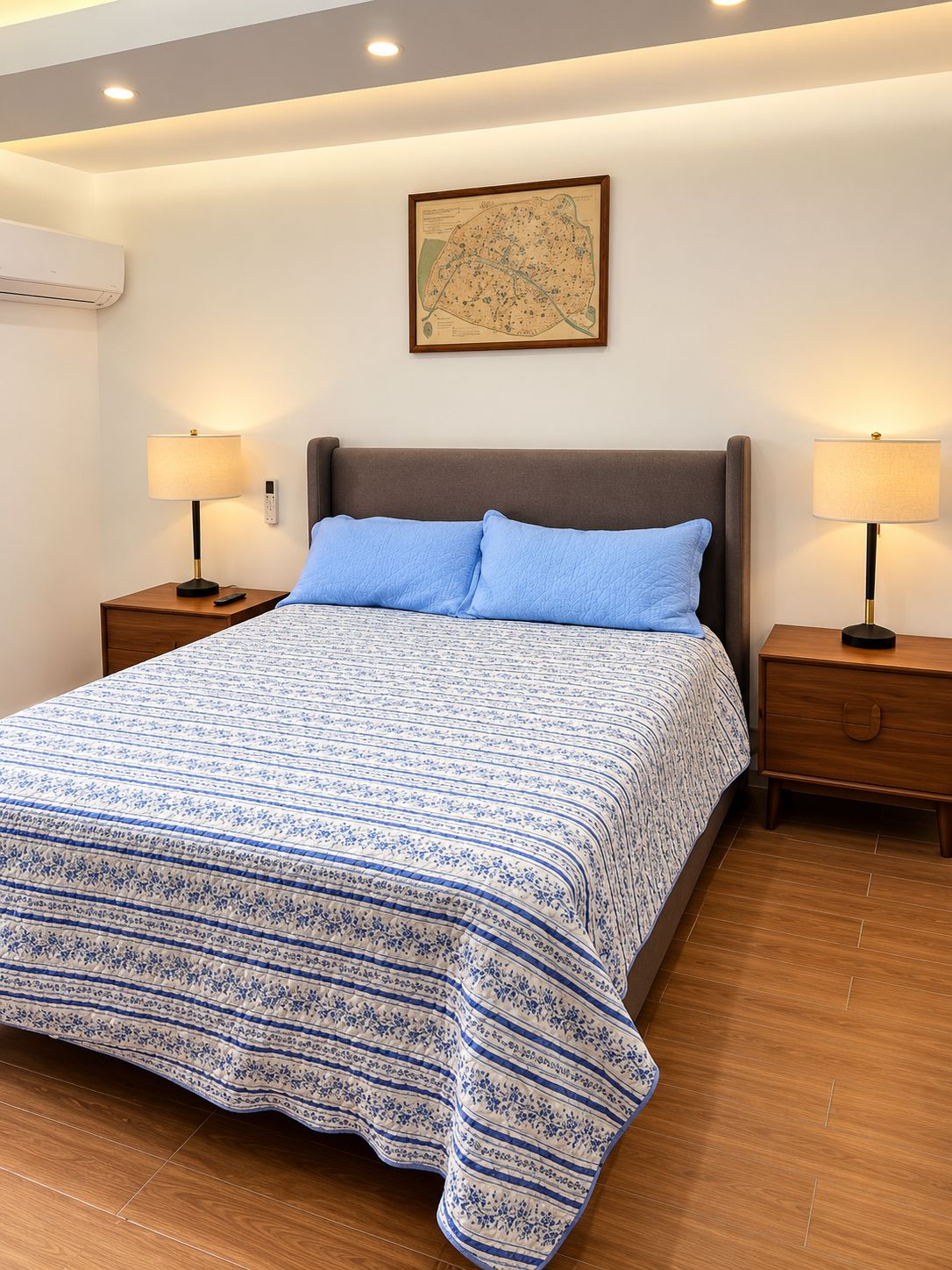 Une chambre à coucher avec un grand lit, deux tables de chevet, un climatiseur fixé au mur et une carte encadrée accrochée au mur.