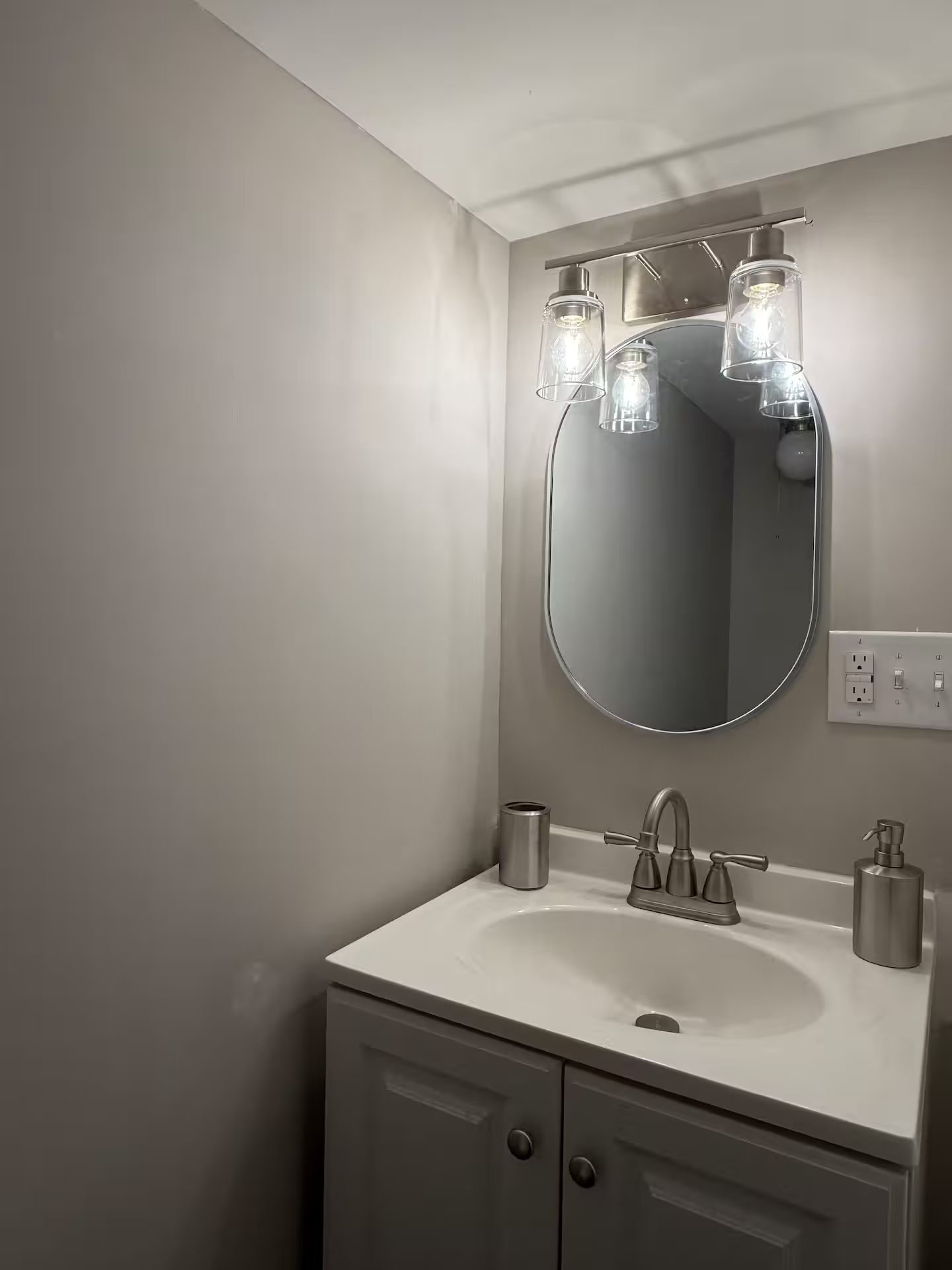 Un bagno con uno specchio rotondo, un lavandino bianco, un rubinetto e tre lampade a sospensione.