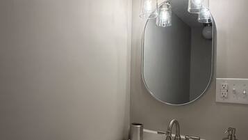 Un bagno con uno specchio rotondo, un lavandino bianco, un rubinetto e tre lampade a sospensione.