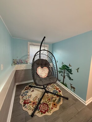 Ein Zimmer mit einem Eckstuhl, einem Teppich mit Blumenmuster und einer Wandmalerei.