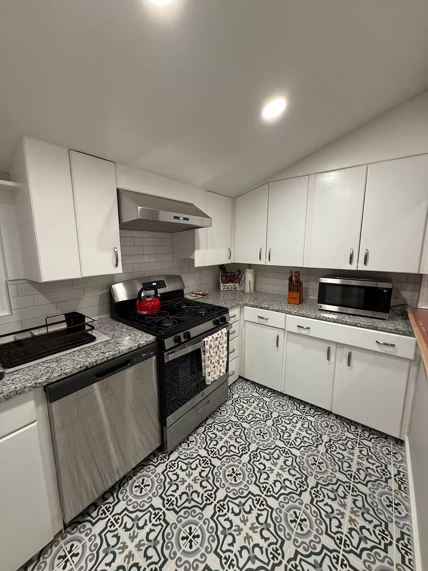 A modern kitchen with white cabinets, a stainless steel stove, a microwave, and patterned floor tiles.