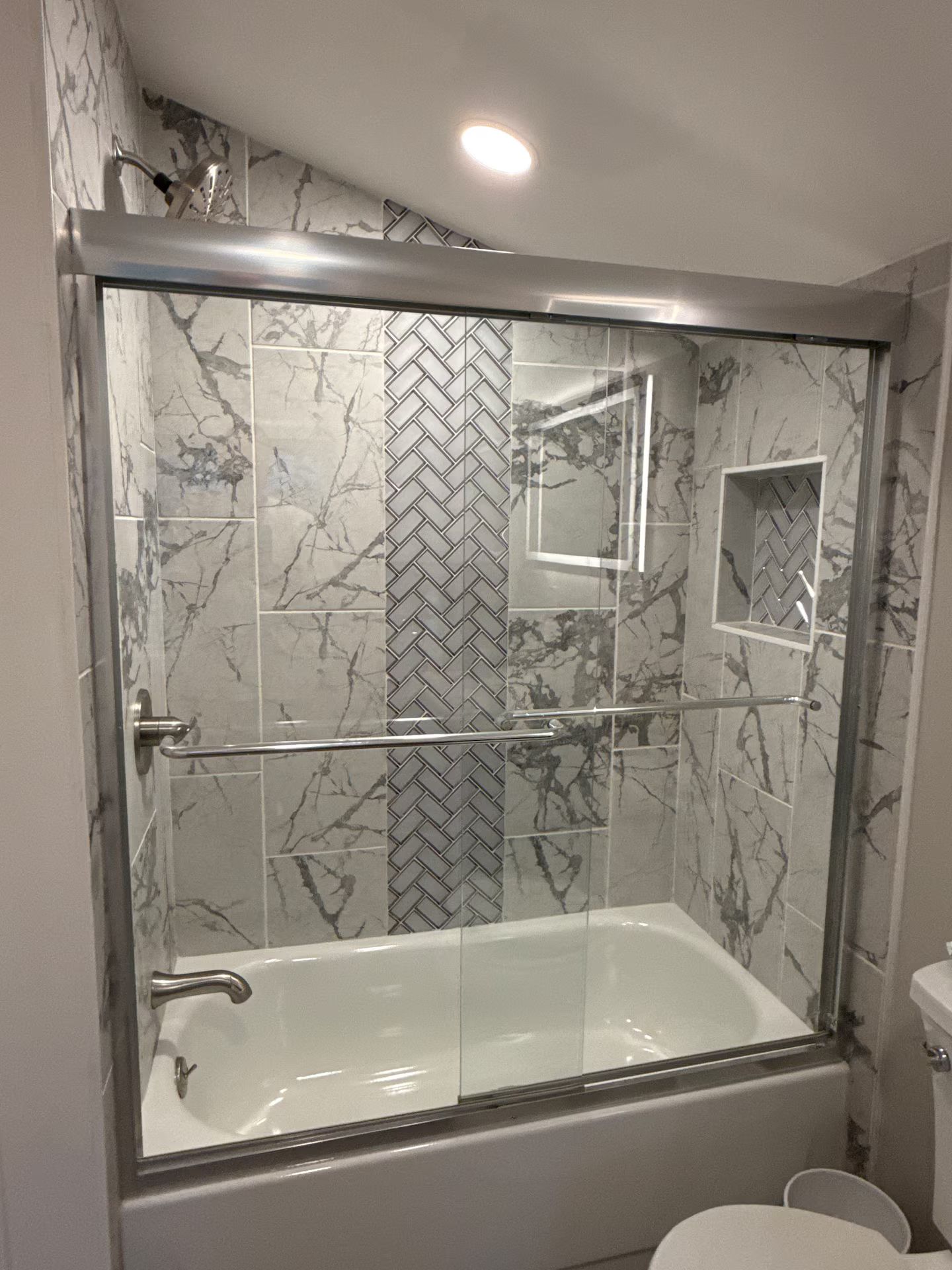 A modern bathroom with a glass-enclosed shower, marble tiles, and a built-in shelf.