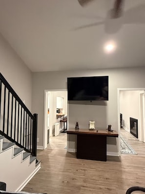 Una sala de estar moderna con un televisor de pantalla plana montado en la pared, una mesa de centro de madera y una escalera con barandillas negras.