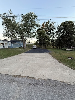 Una entrada residencial con un coche estacionado, árboles y una casa.