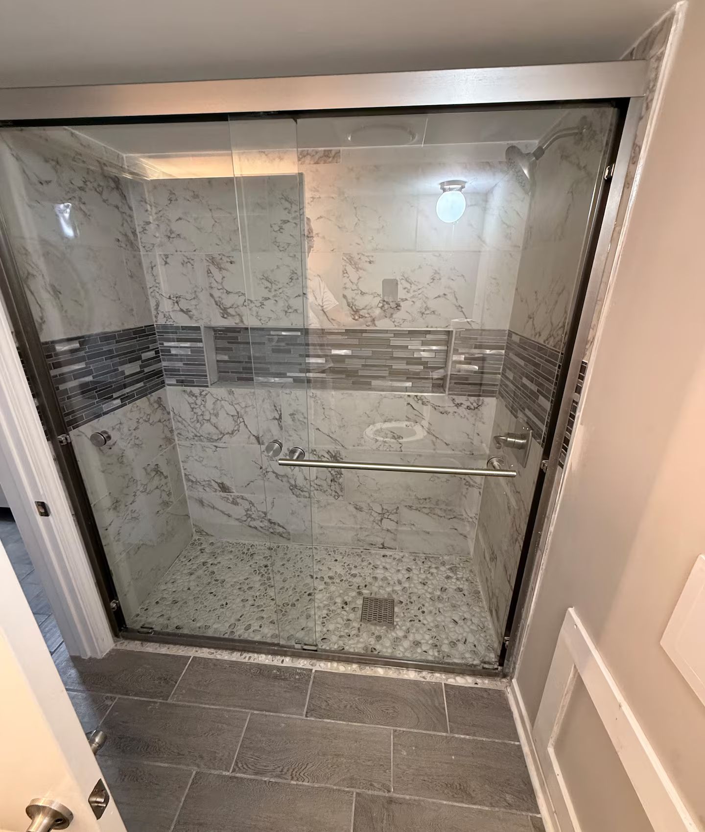A glass-enclosed shower with marble walls and a tiled floor.