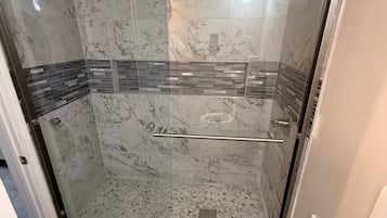 A glass-enclosed shower with marble walls and a tiled floor.