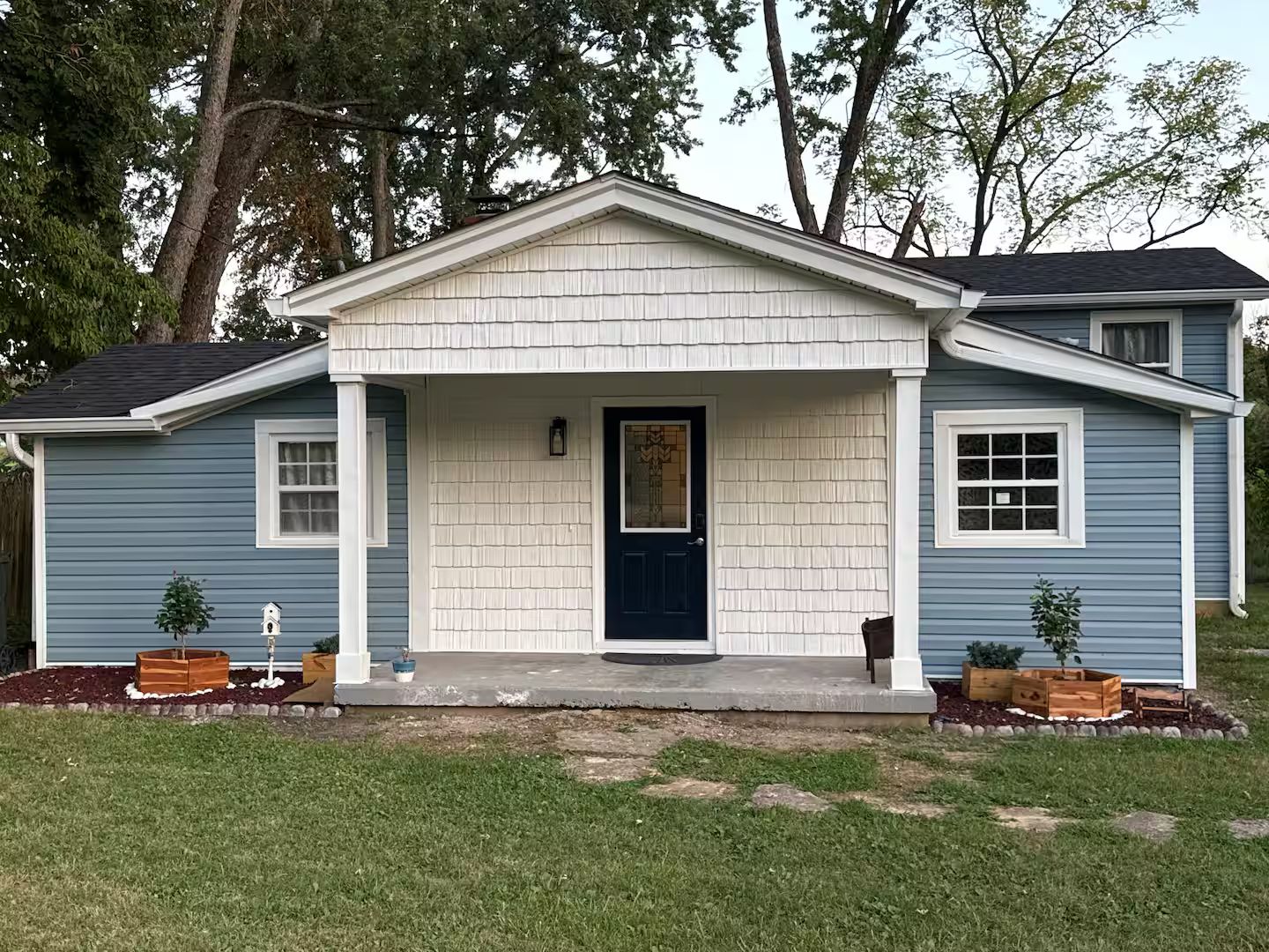 A single-story house with a front porch, a dark blue door, and a small front yard with potted plants.