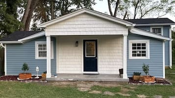 A single-story house with a front porch, a dark blue door, and a small front yard with potted plants.