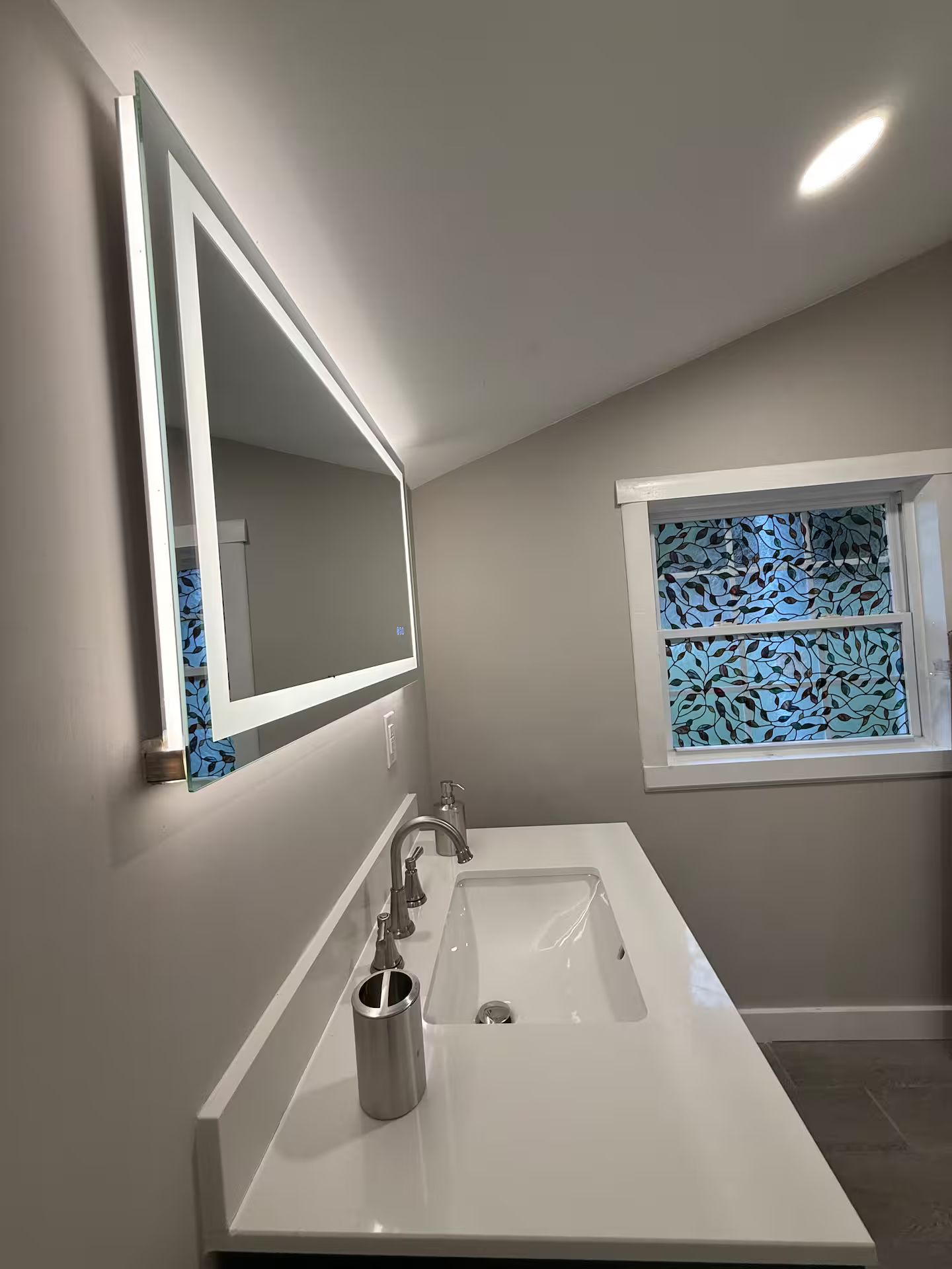 Un baño con un espejo grande, un lavabo y una ventana con diseño de hojas.