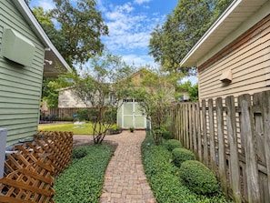 A paved pathway leading to a shed, surrounded by a wooden fence and greenery. - Downtown Secluded Cottage #4 (Pensacola)