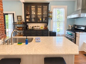 A kitchen with a large island, dark cabinetry, stainless steel appliances, and a brick wall. - Downtown Secluded Cottage #4 (Pensacola)